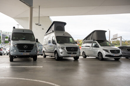 Drei Mercedes-Benz Camper stehen mit aufgeklappten Dächern nebeneinander unter einem überdachten Bereich.
