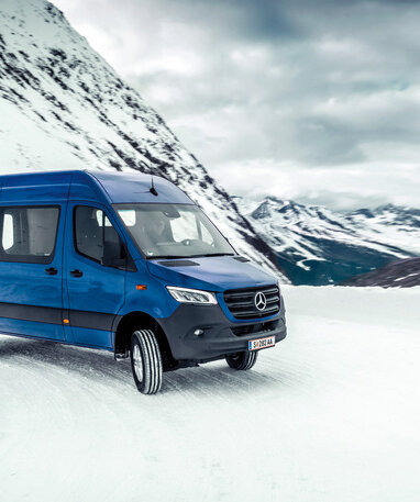 Ein blauer Mercedes-Benz Transporter fährt durch schneebedeckte Berglandschaft.