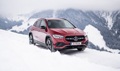 Ein roter Mercedes-Benz GLA auf einer verschneiten Straße mit Bergkulisse.