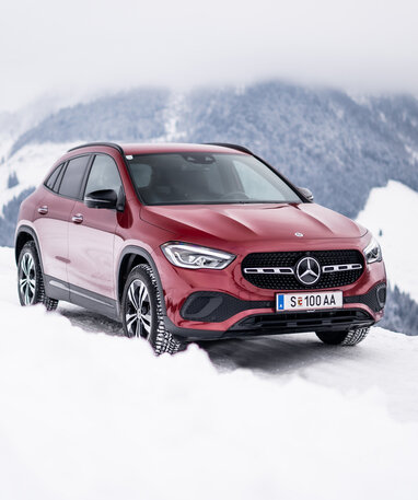 Ein roter Mercedes-Benz GLA auf einer verschneiten Straße mit Bergkulisse.