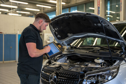 Ein Mechaniker überprüft den Motor eines Mercedes mit einem Tablet.