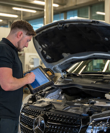 Ein Mechaniker überprüft den Motor eines Mercedes mit einem Tablet.