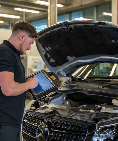 Ein Mechaniker überprüft den Motor eines Mercedes mit einem Tablet.