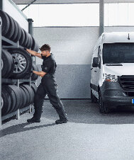 Ein Mechaniker stapelt Reifen in einem Lager neben einem weißen Lieferwagen.