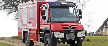 Ein roter Feuerwehr-Unimog fährt auf einem Feldweg.