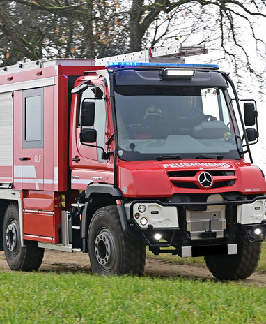 Ein roter Feuerwehr-Unimog fährt auf einem Feldweg.