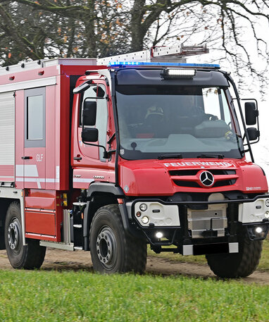 Ein roter Feuerwehr-Unimog fährt auf einem Feldweg.
