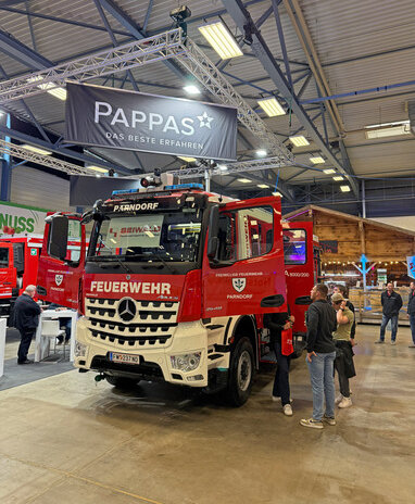 Ein Feuerwehr-Lkw der Freiwilligen Feuerwehr Parndorf bei einer Messe ausgestellt, mit dem Logo von Pappas im Hintergrund.