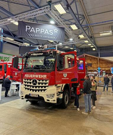 Ein Feuerwehr-Lkw der Freiwilligen Feuerwehr Parndorf bei einer Messe ausgestellt, mit dem Logo von Pappas im Hintergrund.
