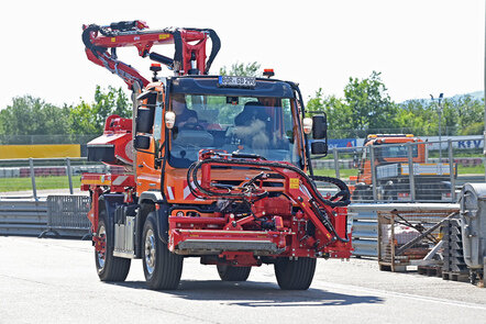 Ein oranger Unimog mit einem roten Mäharm fährt auf einer Straße.