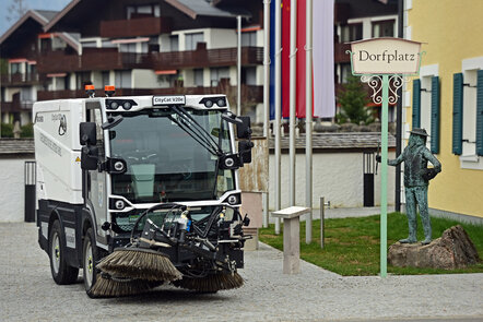 Eine Straßenkehrmaschine der Marke CityCat vor einem Schild mit der Aufschrift 'Dorfplatz'.