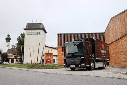 Der Mercedes-Benz eEconic mit dem Logo der Trumer Brauerei vor dem Gebäude der Brauerei.
