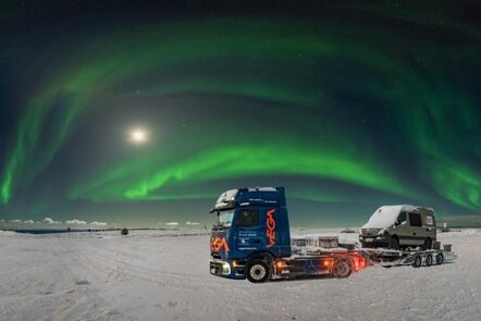 Blauer eActros600 mit orangem VEGA-Logo mit Sattelzug auf einer schneebedeckten Fläche unter grünem Polarlicht.