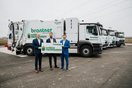 Drei Männer präsentieren Schilder vor elektrischen Müllfahrzeugen. | © 2026 Johannes Vogl, all rights reserved.