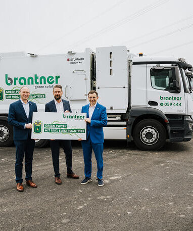 Drei Männer präsentieren Schilder vor elektrischen Müllfahrzeugen. | © 2026 Johannes Vogl, all rights reserved.