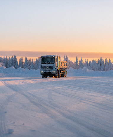 Ein eArocs400 fährt bei Sonnenuntergang auf einer verschneiten Straße durch eine winterliche Landschaft.