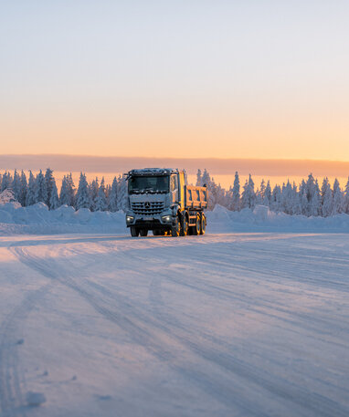 Ein eArocs400 fährt bei Sonnenuntergang auf einer verschneiten Straße durch eine winterliche Landschaft.