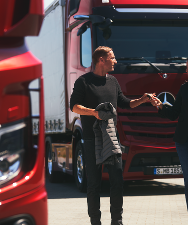 Zwei Personen unterhalten sich vor roten Mercedes-Benz Actros L.