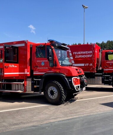 Zwei rote Unimog Feuerwehrfahrzeuge der Feuerwehr Zurndorf stehen nebeneinander.