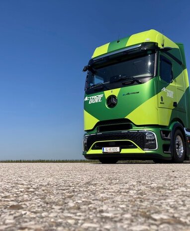 Ein grüner Mercedes-Benz eActros auf einer asphaltierten Fläche unter blauem Himmel.