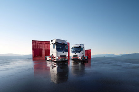 Zwei Mercedes-Benz Trucks stehen vor einem roten Container auf einer spiegelnden Fläche.