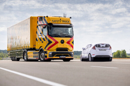Gelber Mercedes-Benz Safety Truck auf der Straße mit Pkw daneben.