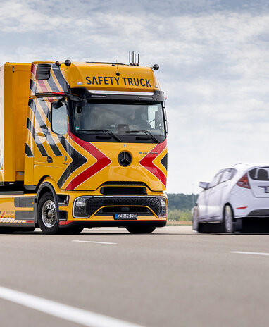 Gelber Mercedes-Benz Safety Truck auf der Straße mit Pkw daneben.