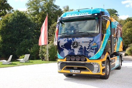 Ein elektrischer Mercedes-Benz Lkw mit Weltkarten-Design und der Aufschrift 'ELECTRIC' steht neben einer Fahne.