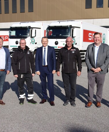 Sechs Männer stehen vor mehreren SPAR-Lkw auf einem Lagerhof.