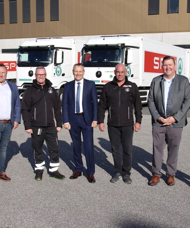 Sechs Männer stehen vor mehreren SPAR-Lkw auf einem Lagerhof.