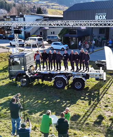 Gruppe von Menschen steht auf einem Lastwagen bei einer Veranstaltung im Freien.