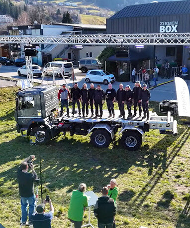 Gruppe von Menschen steht auf einem Lastwagen bei einer Veranstaltung im Freien.