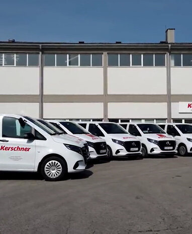 6 weiße Vito Tourer mit Kerschner-Branding stehen nebeneinander vor dem Kerschner Firmengebäude.