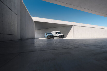 Zwei moderne Vans parken in einer minimalistischen, grauen Architektur.