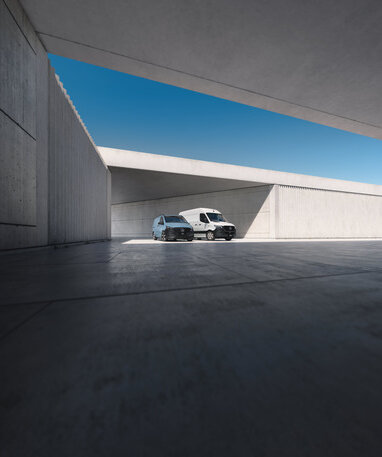 Zwei moderne Vans parken in einer minimalistischen, grauen Architektur.