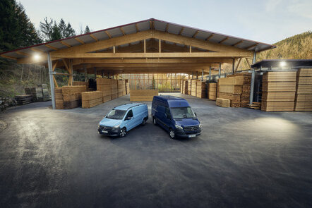 Zwei Mercedes-Benz Transporter parken vor einer Holzlagerhalle.