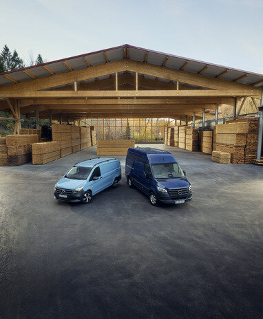 Zwei Mercedes-Benz Transporter parken vor einer Holzlagerhalle.