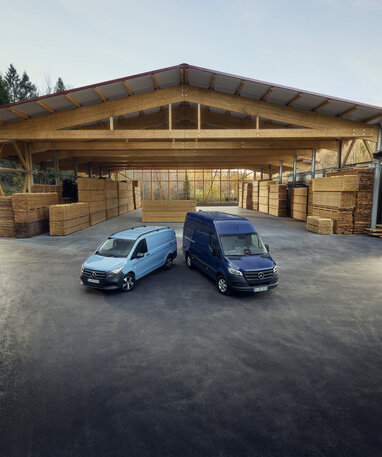 Zwei Mercedes-Benz Transporter parken vor einer Holzlagerhalle.