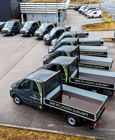 Reihe von Mercedes-Benz Sprinter Pritschenwagen mit der Aufschrift 'Wir pflanzen Zukunft'.