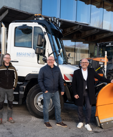 Vier Männer stehen vor einem weißen Unimog mit Schneepflug, bereit für den Winterdienst.