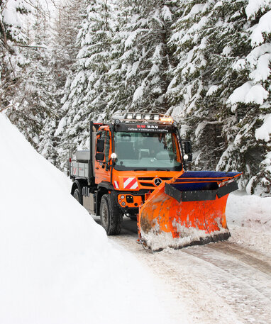 Ein orangefarbener Schneepflug räumt eine schneebedeckte Straße frei.