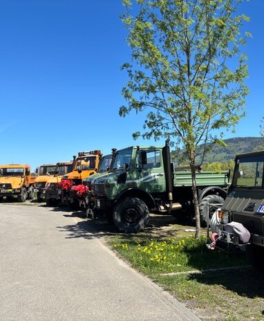 Verschiedene Unimog-Fahrzeuge geparkt unter blauem Himmel.