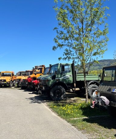 Verschiedene Unimog-Fahrzeuge geparkt unter blauem Himmel.