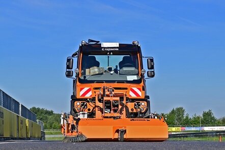 Eine orangefarbene Unimog mit Kehraufsatz von Kahlbacher auf einer Straße.