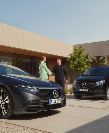 Ein Kunde begrüßt einen Mitarbeiter von Mercedes-Benz vor einem Gebäude. Ein Mercedes-Benz EQ Auto und ein Lieferwagen sind zu sehen.