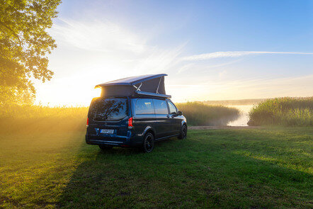 Ein blauer Mercedes-Benz Marco Polo mit Aufstelldach parkt auf einer Wiese am Ufer eines Sees im Morgenlicht. | © Mercedes-Benz Österreich