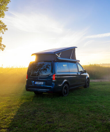 Ein blauer Mercedes-Benz Marco Polo mit Aufstelldach parkt auf einer Wiese am Ufer eines Sees im Morgenlicht. | © Mercedes-Benz Österreich