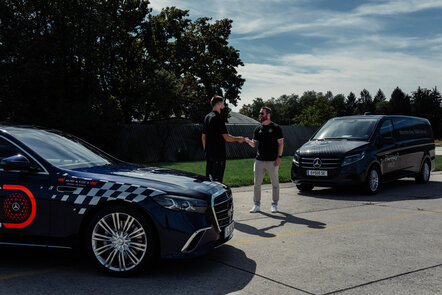 Zwei Männer stehen neben zwei Mercedes-Benz Fahrzeugen und schütteln sich die Hände.