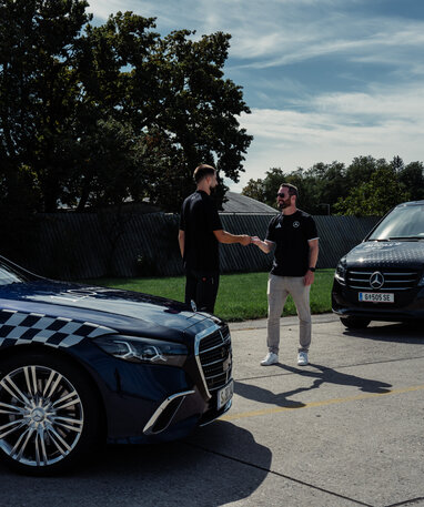 Zwei Männer stehen neben zwei Mercedes-Benz Fahrzeugen und schütteln sich die Hände.