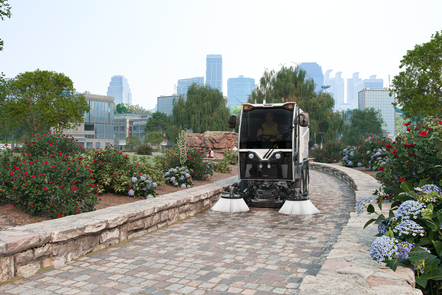Eine CityCat VR17e Kehrmaschine von Bucher kehrt einen Gehweg in einem Park.